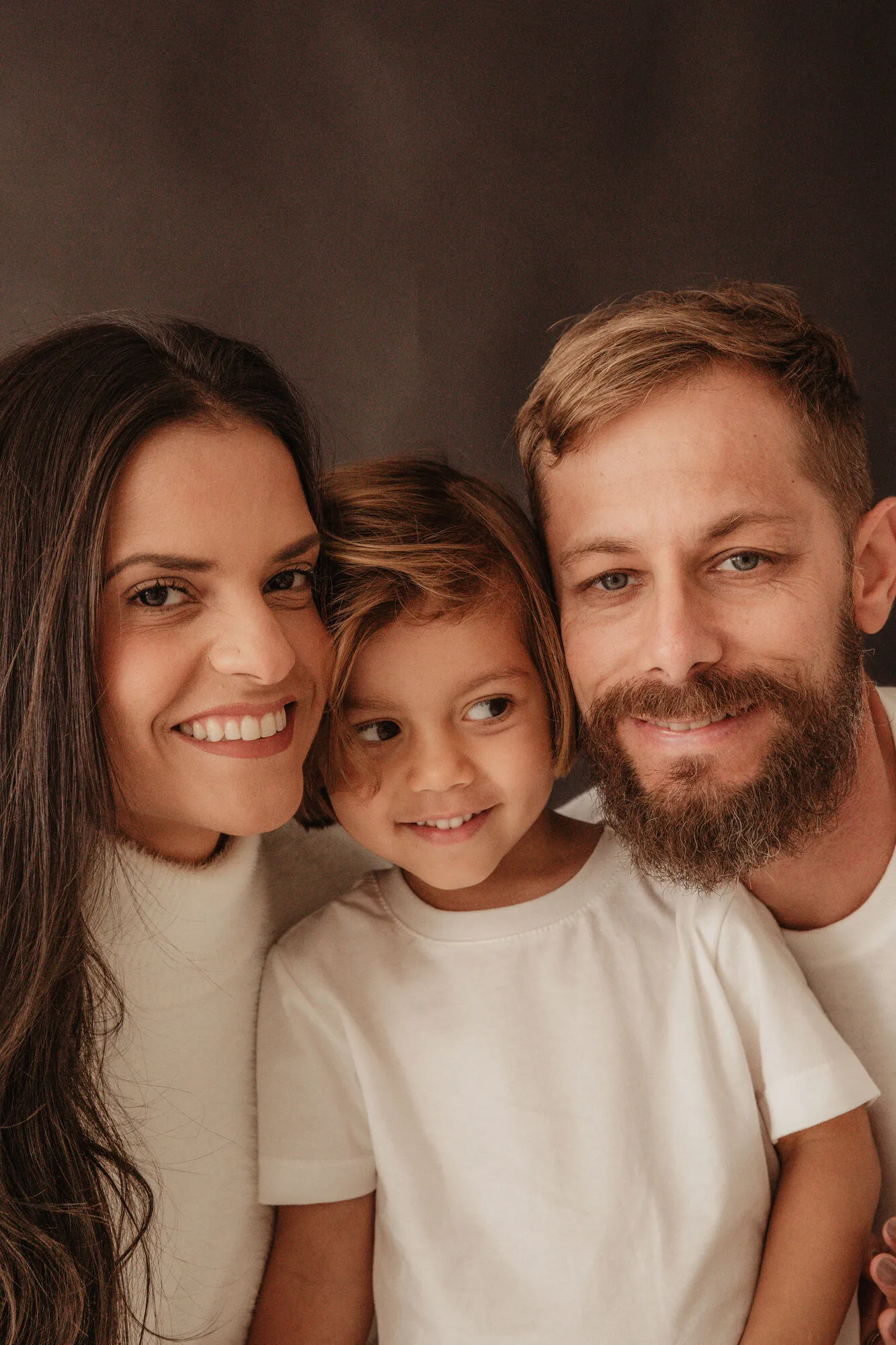 Retrato de família — pai, mãe e filho juntos em fundo escuro durante ensaio