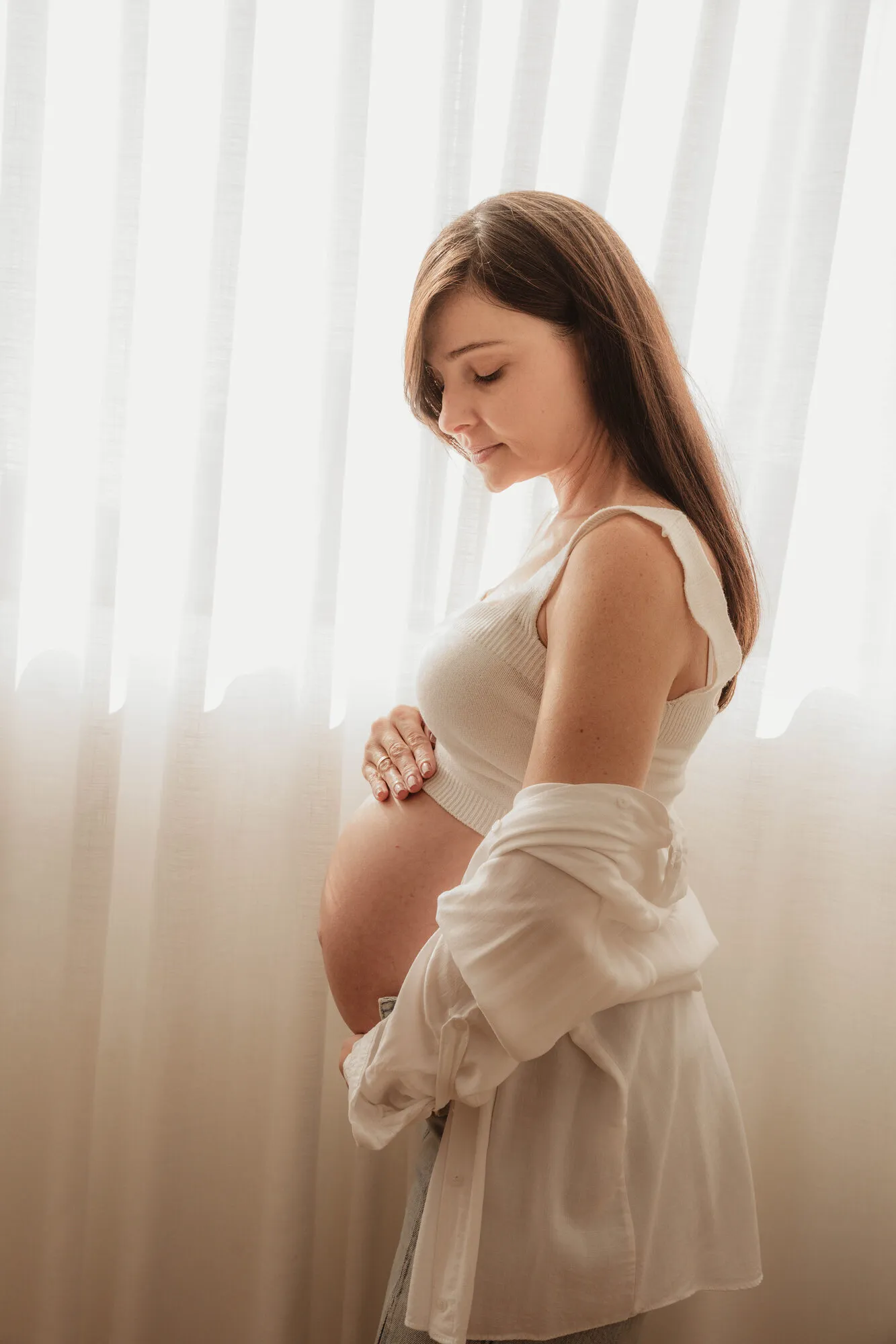 Gestante de perfil na luz da janela segurando a barriga